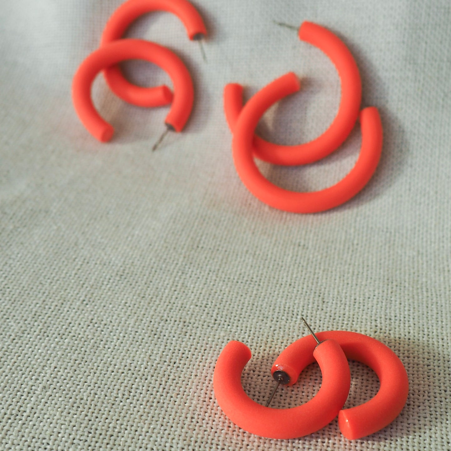 three pairs of coral hoop earrings of various sizes on a white textured fabric background