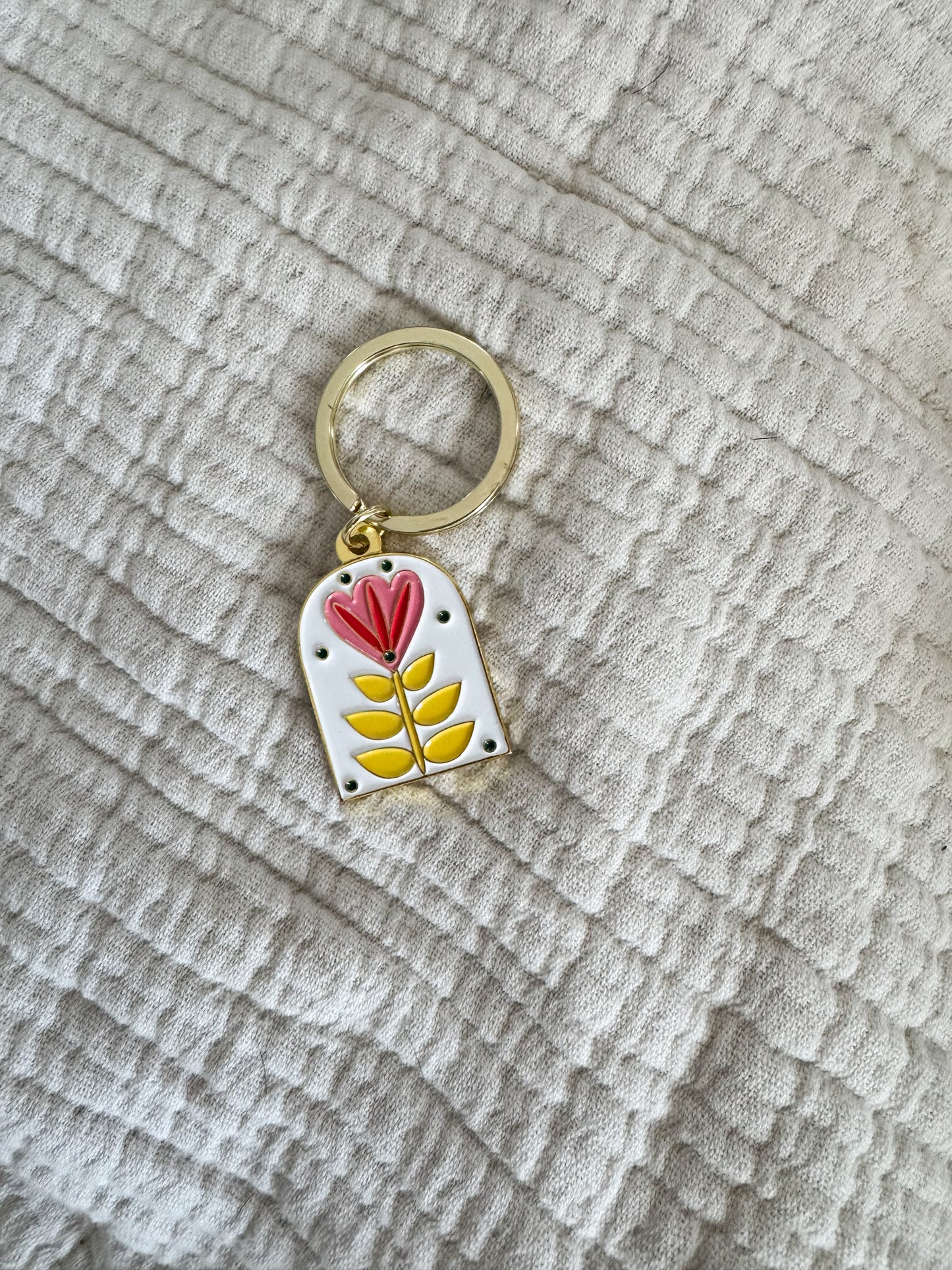 white enamel keychain with floral design and gold ring on a cream fabric background