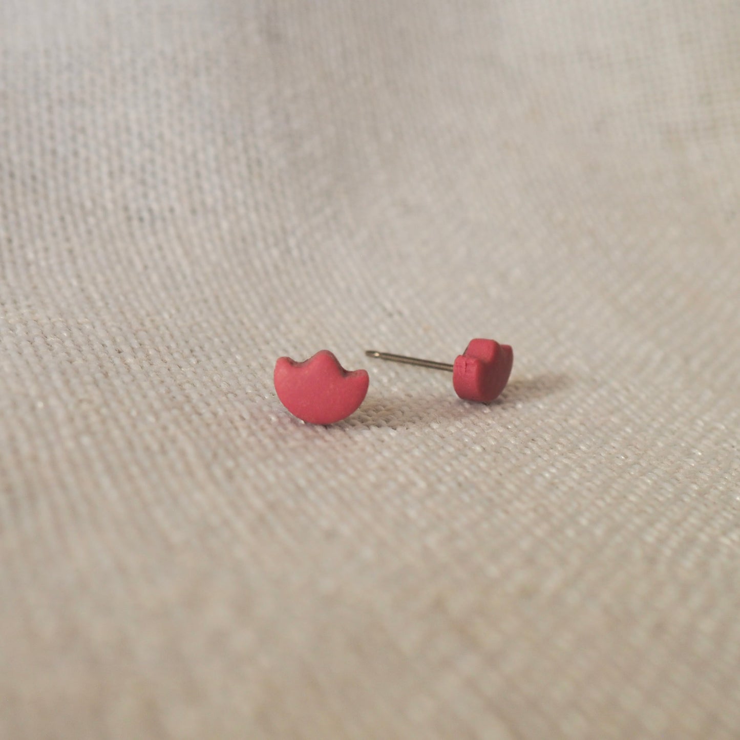 Light cranberry polymer clay tulip top stud earrings set on white textured backdrop