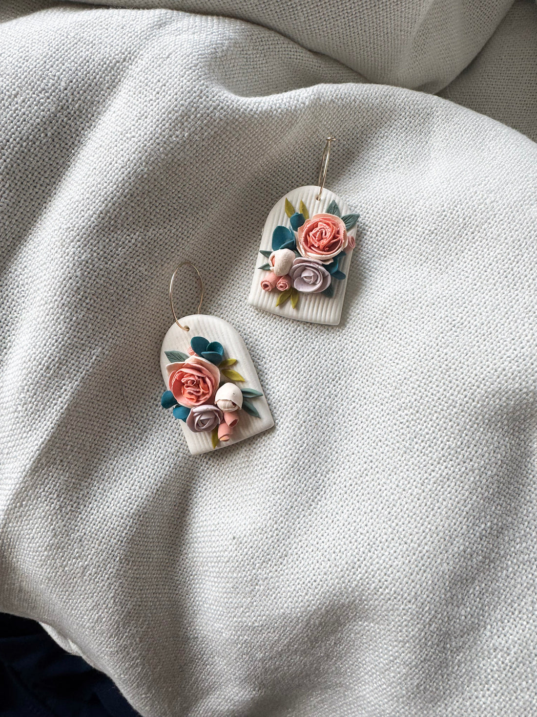 pair of arch-shaped floral earrings with peach and blue florals on a cream background
