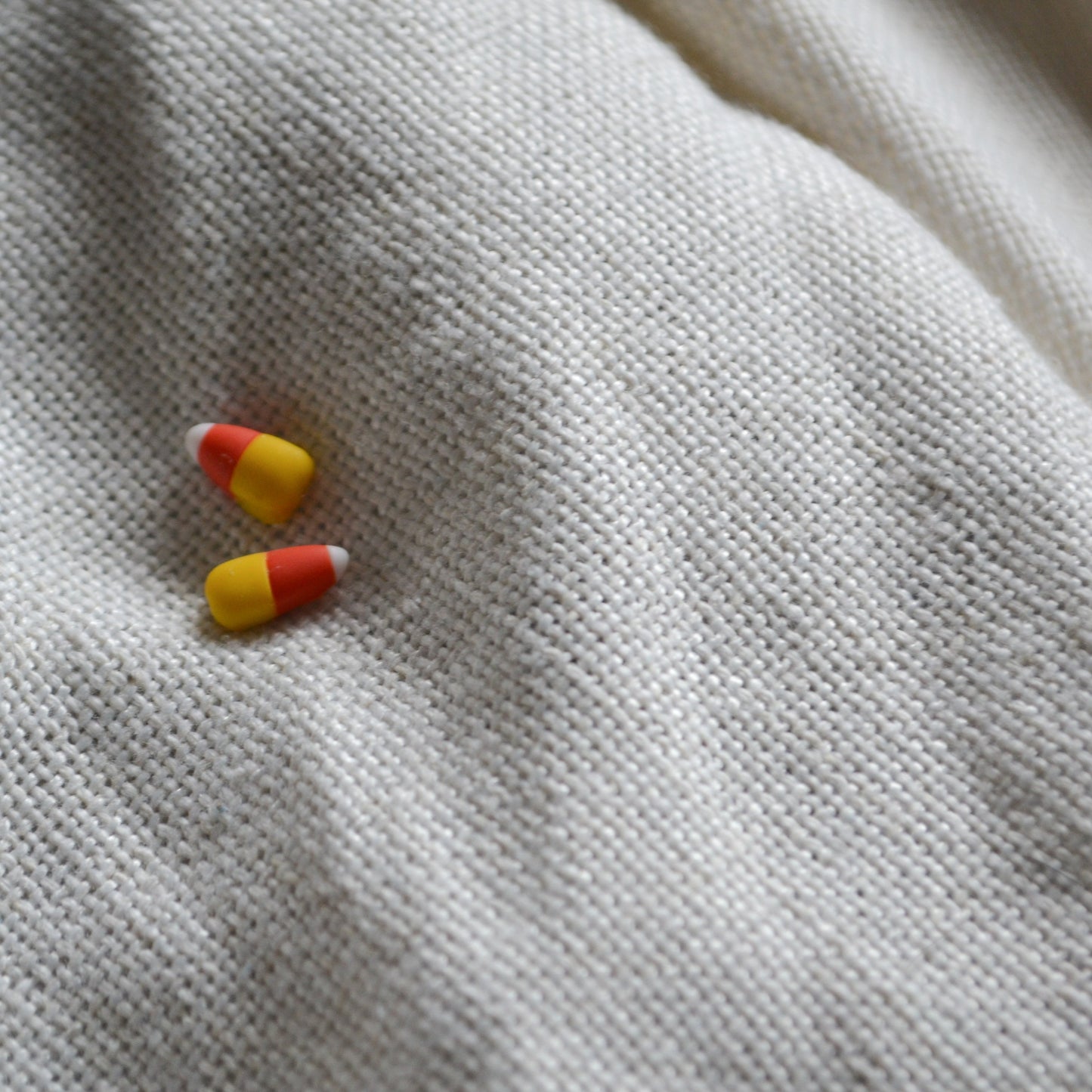 a pair of candy corn stud earrings flat on a cream background