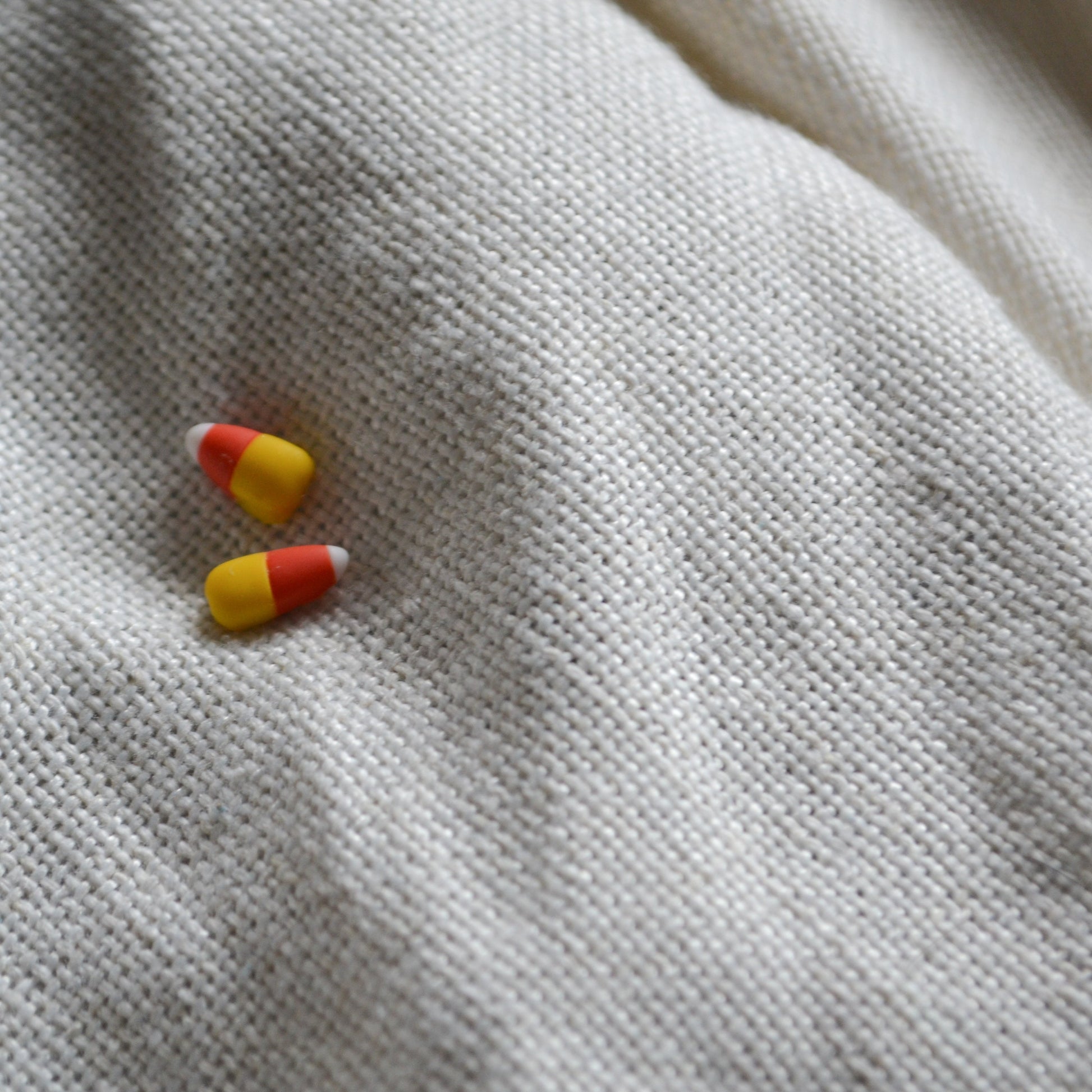 a pair of candy corn stud earrings flat on a cream background