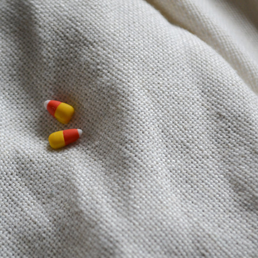 a pair of candy corn stud earrings flat on a cream background
