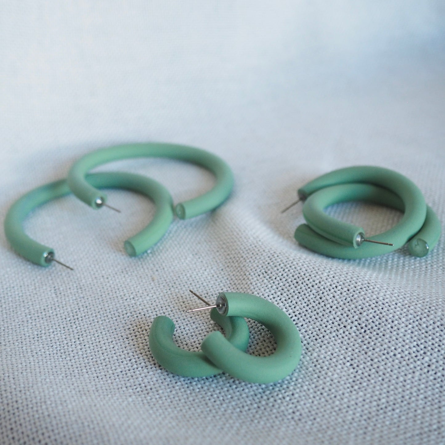 Various sized aloe green polymer clay hoops set on a white textured background. 