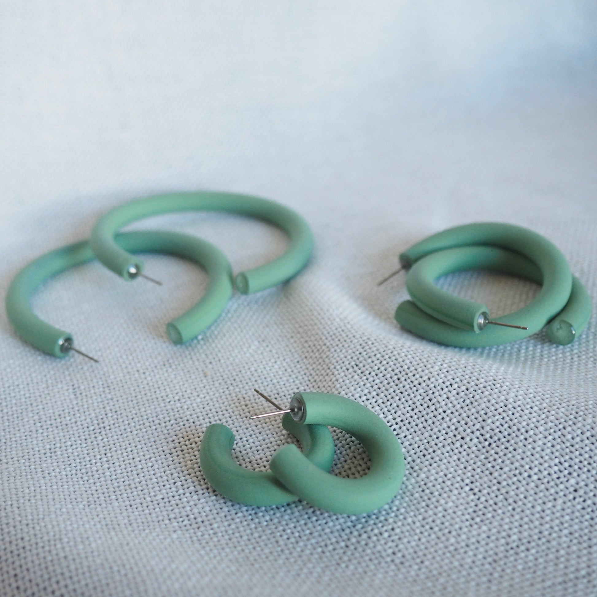 Various sized aloe green polymer clay hoops set on a white textured background. 