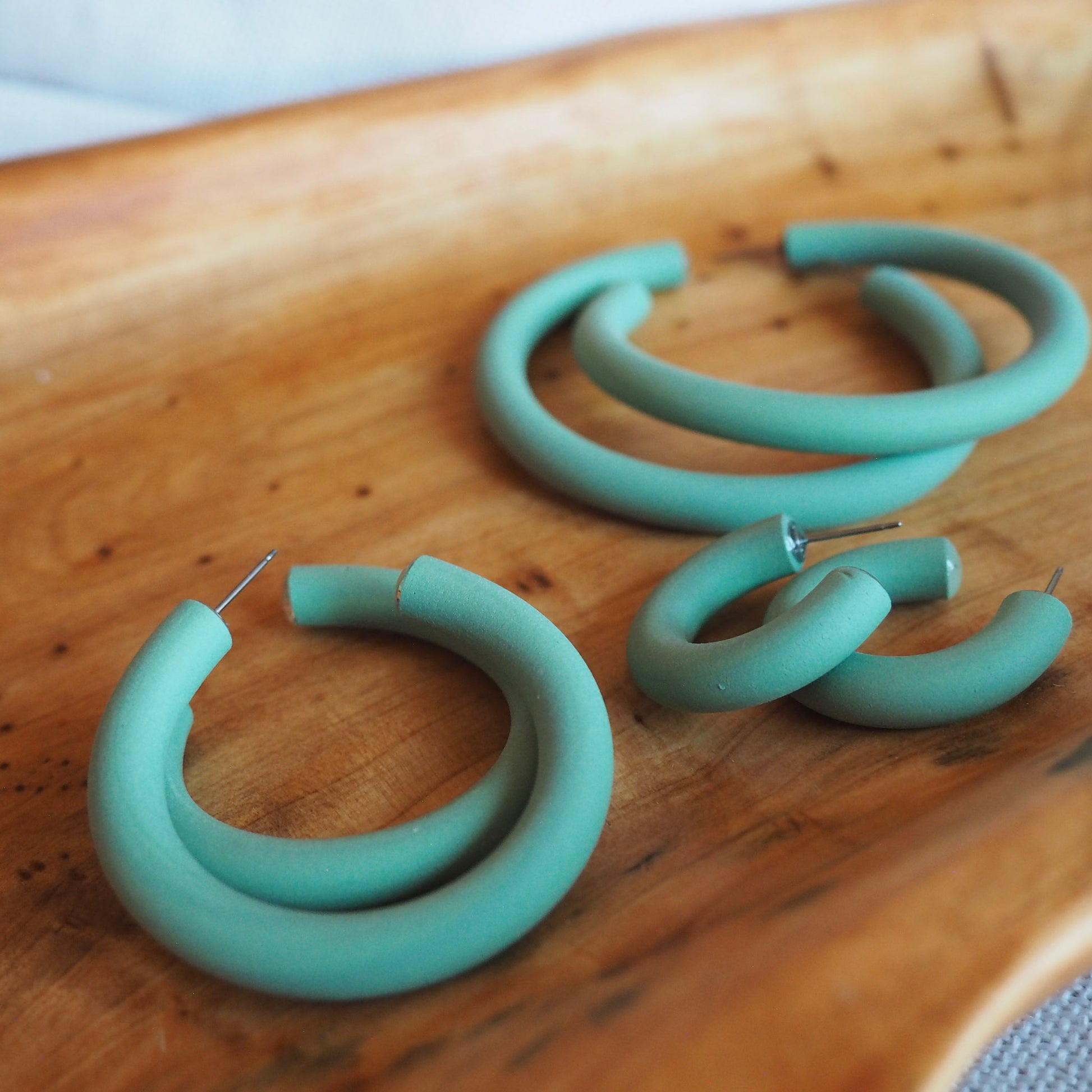 Various sized aloe green polymer clay hoops set on wooden tray on a white textured background. 