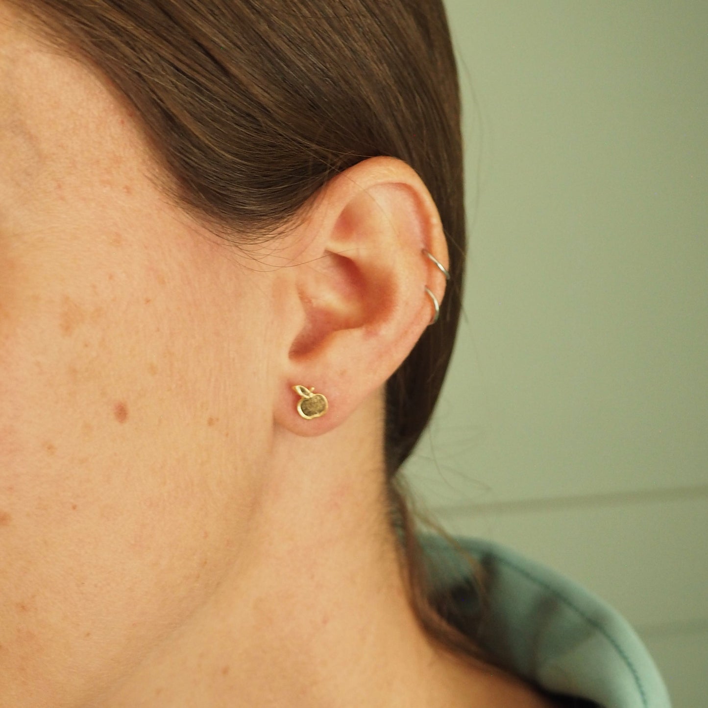 Model wearing small gold apple stud with green background