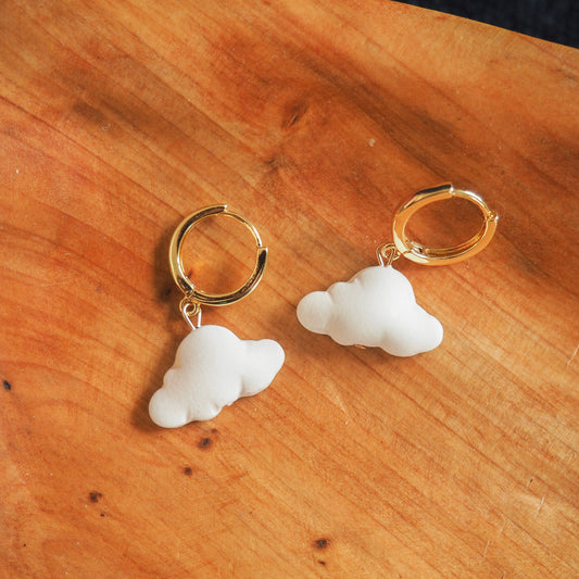 White cloud polymer clay earrings with gold huggies set on a wooden background
