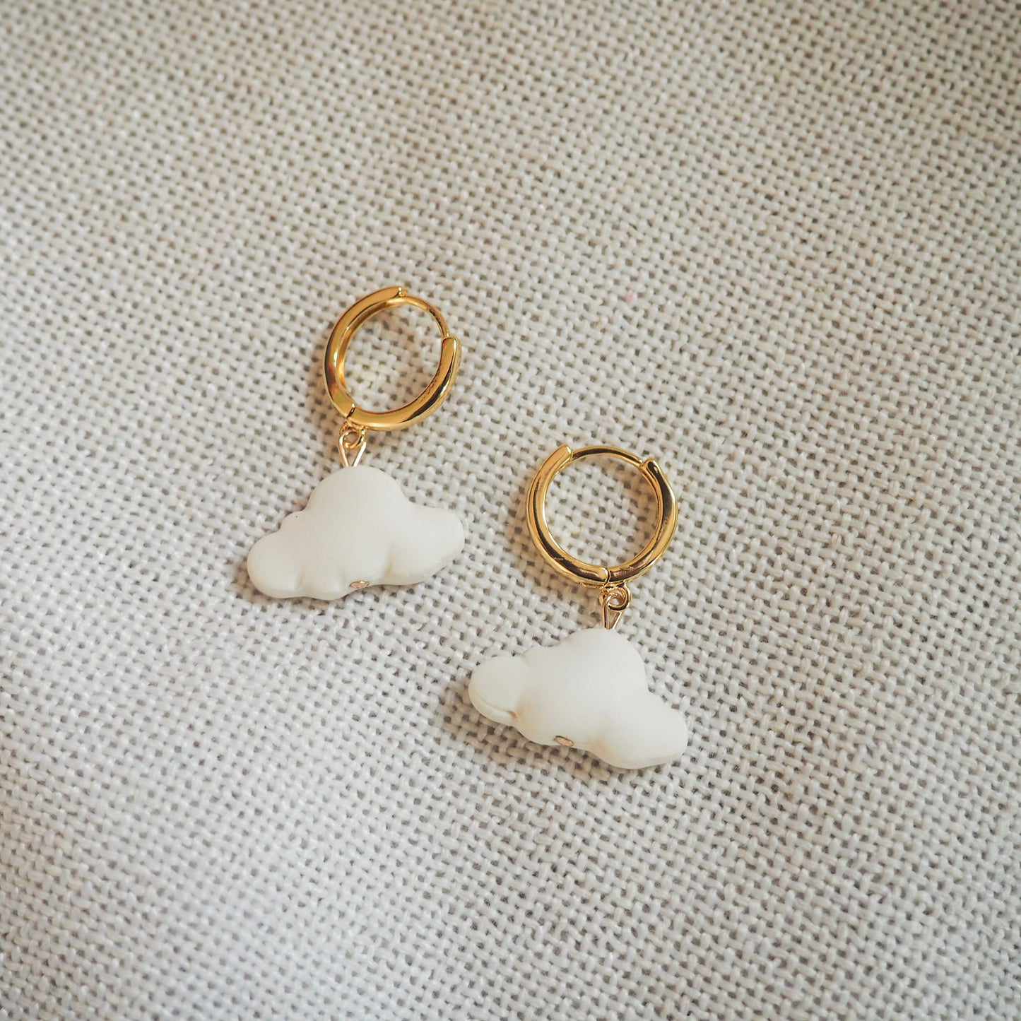 White cloud polymer clay earrings with gold huggies set on a white textured background