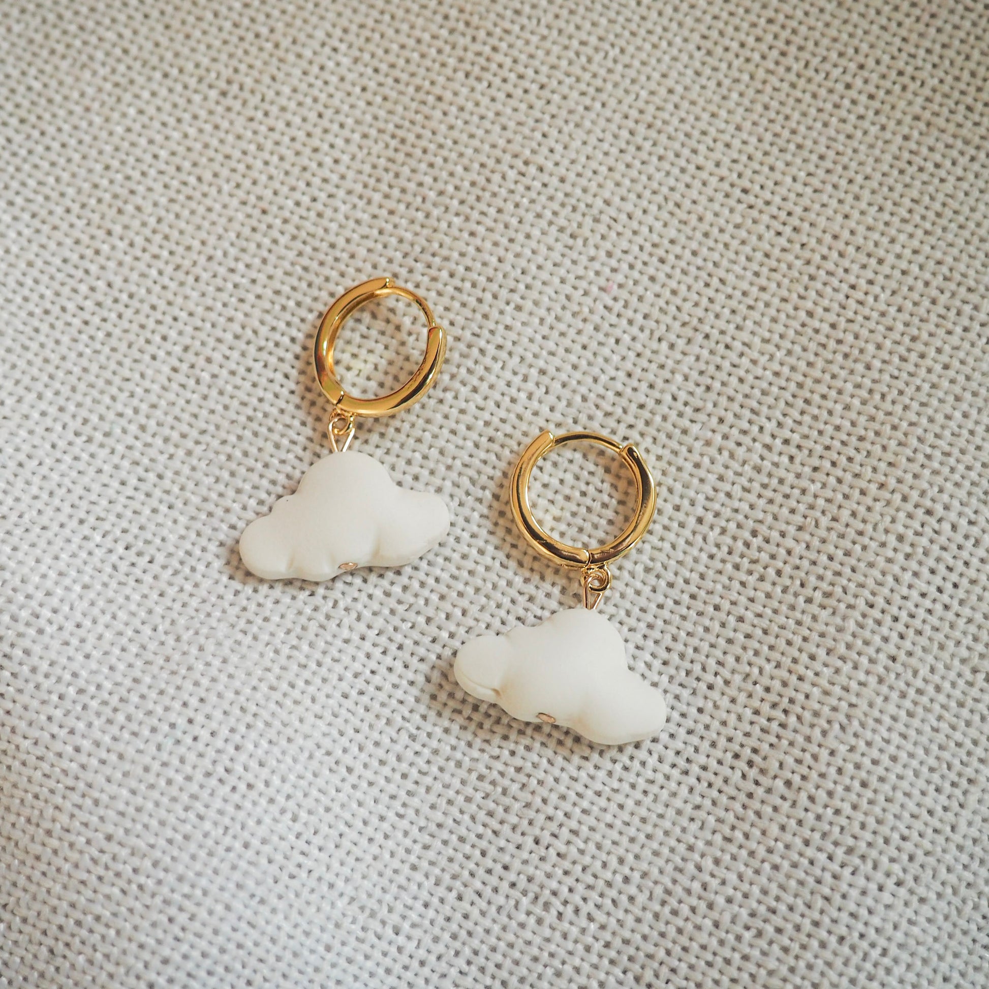 White cloud polymer clay earrings with gold huggies set on a white textured background