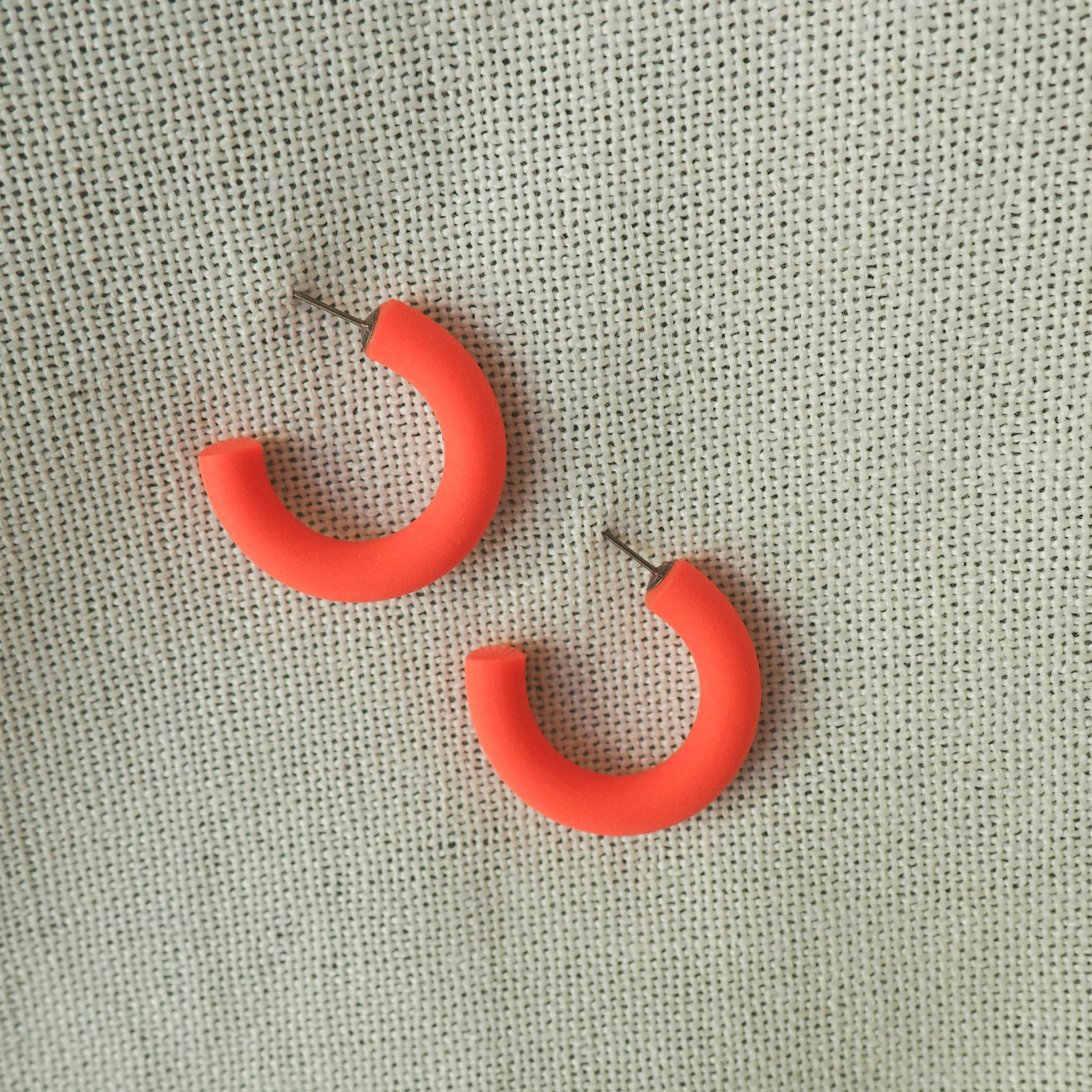 small coral hoop earrings white textured fabric background