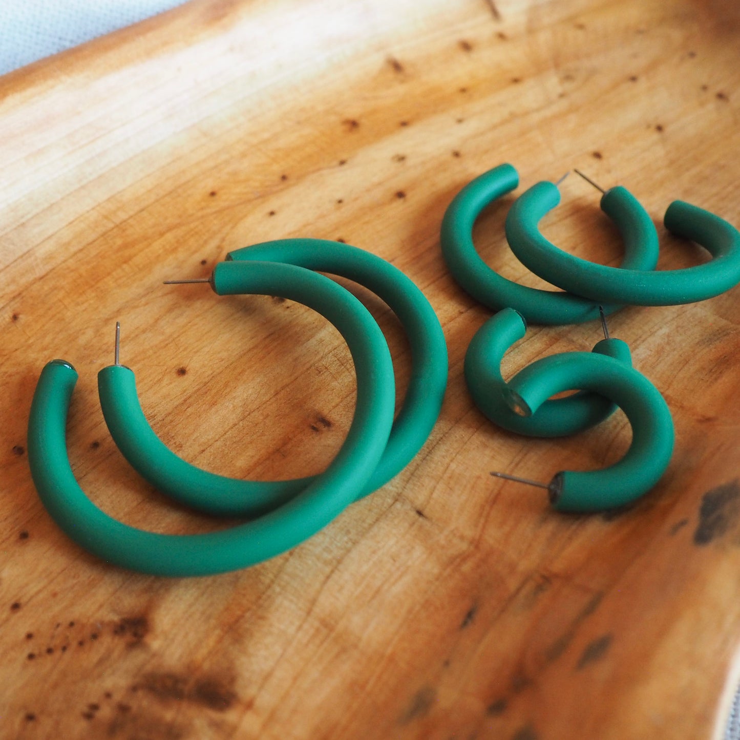 Various sized emerald green polymer clay hoops set on wooden tray on a white textured background. 