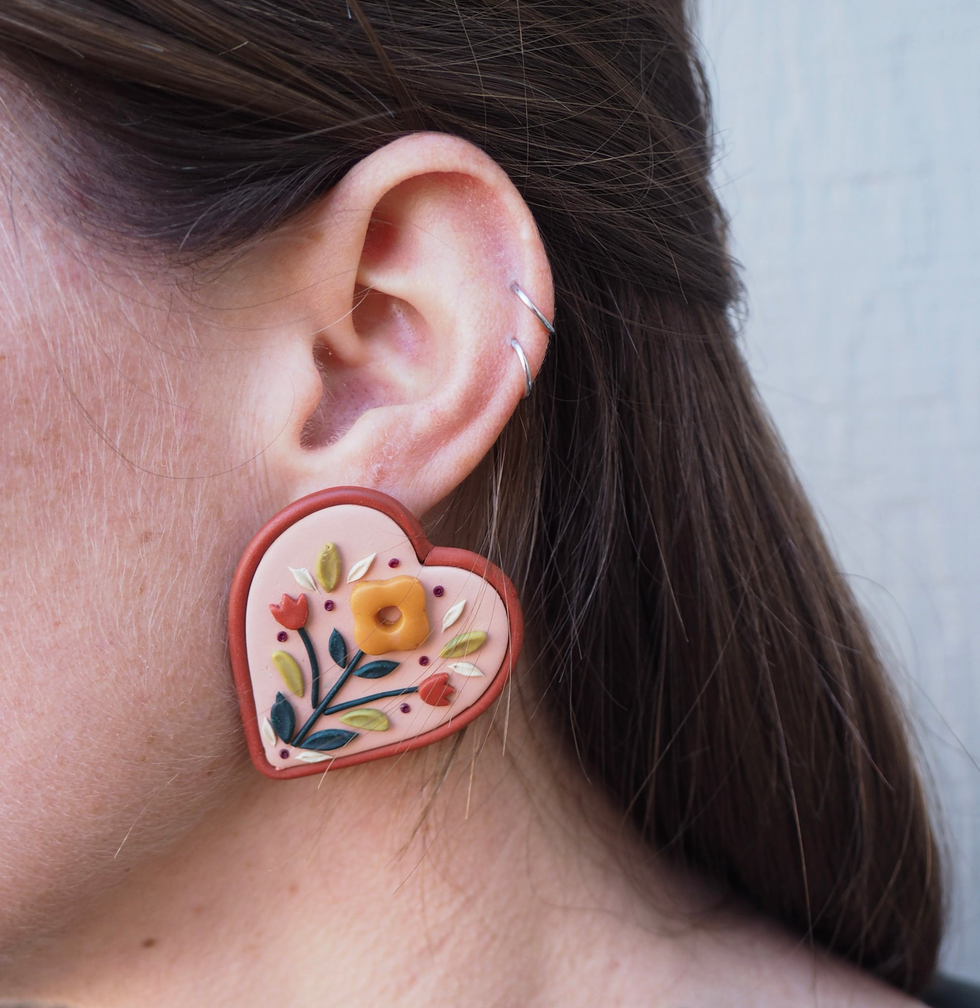 model wearing Folk style and heart shaped clay floral earring with warm terra cotta colors