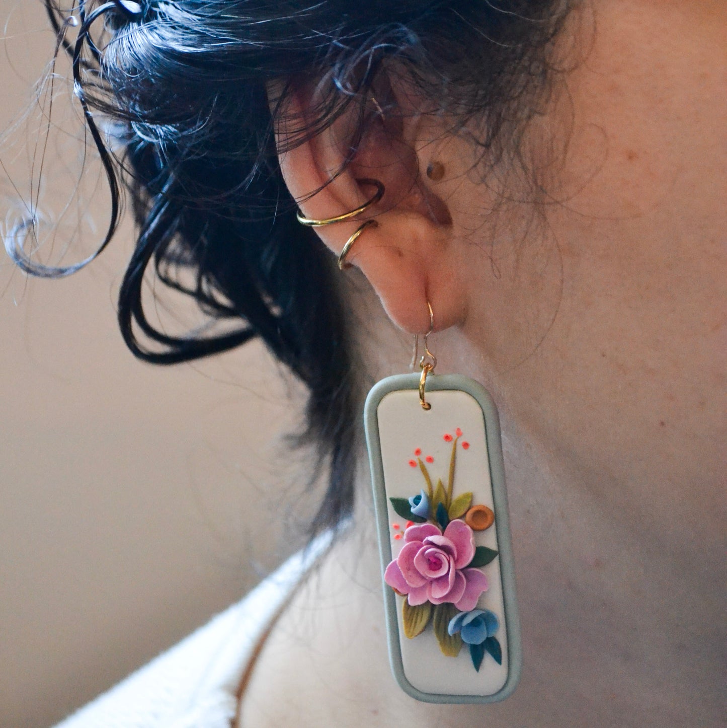 model wearing pink and blue florals earrings with orange and green accents on a light blue rectangle background with gold fish hooks