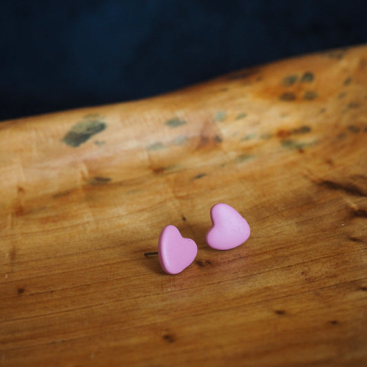 light pink clay stud earrings that are heart-shaped and sitting on a wooden background