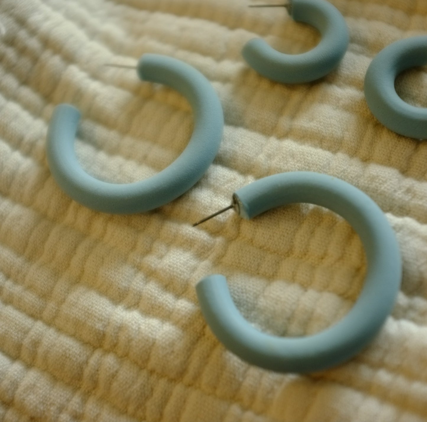 smaller light blue hoop earrings with post studs on a textured fabric background