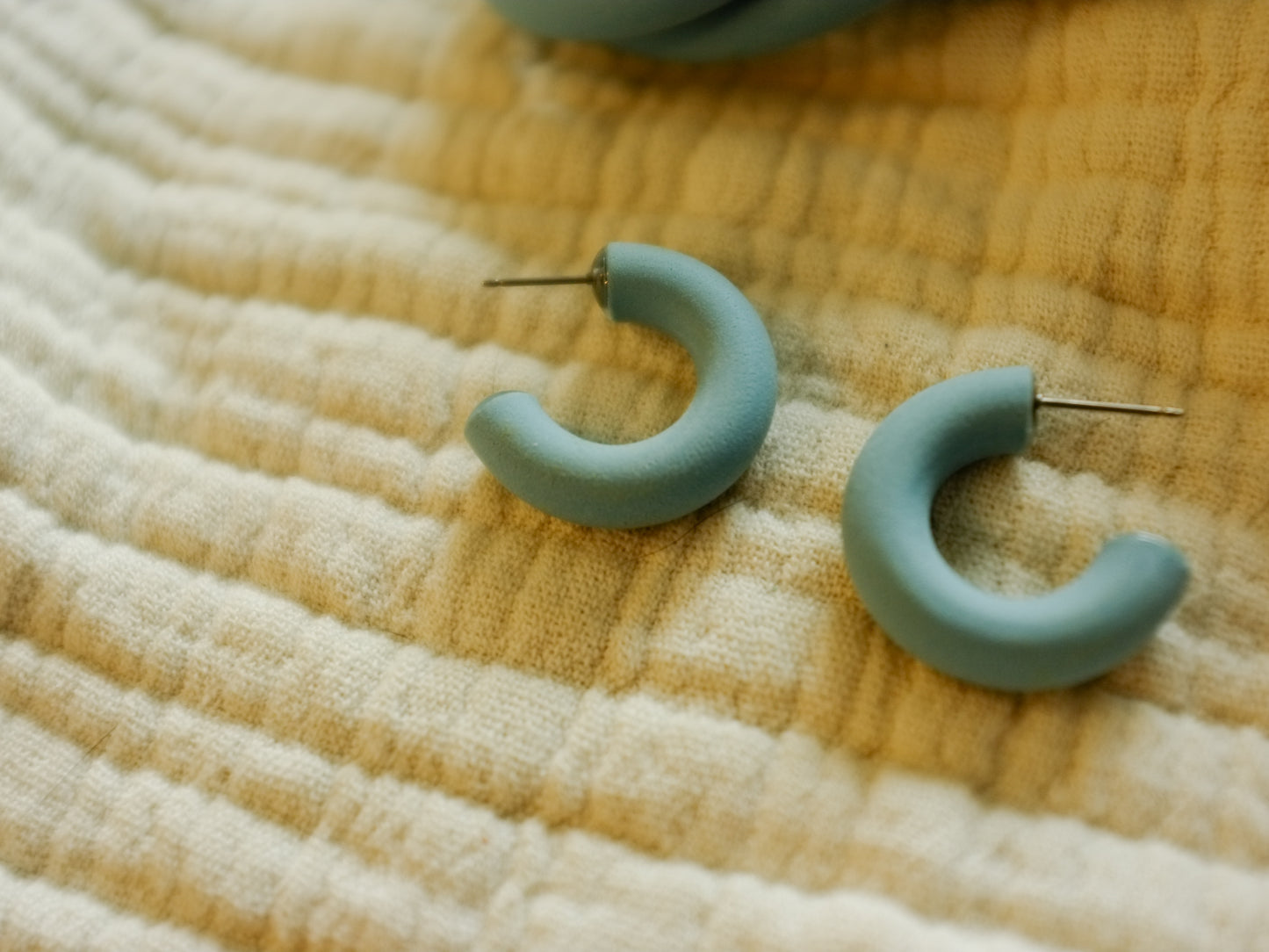 small light blue hoop earrings with post studs on a textured fabric background