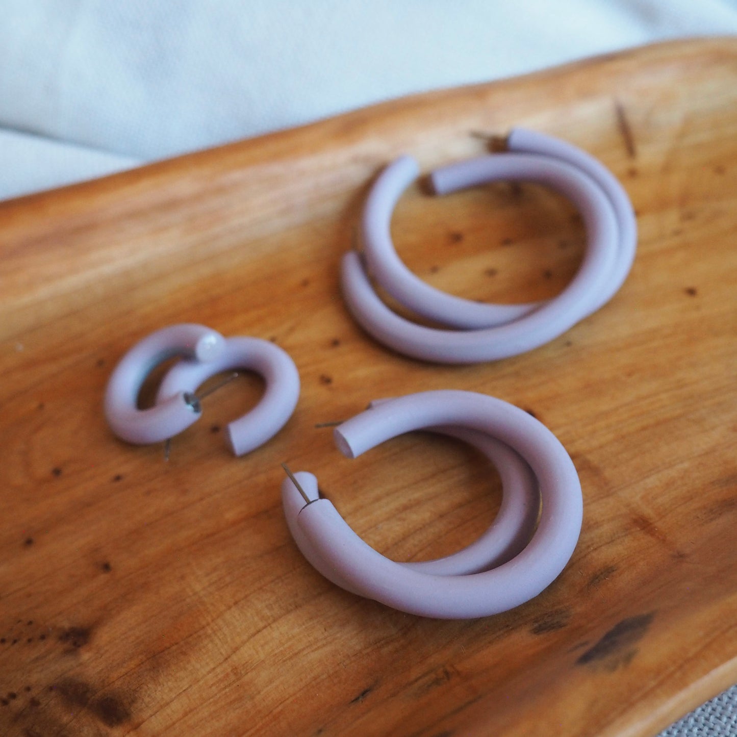 Various sized  lavender polymer clay hoops set on wooden tray on a white textured background. 