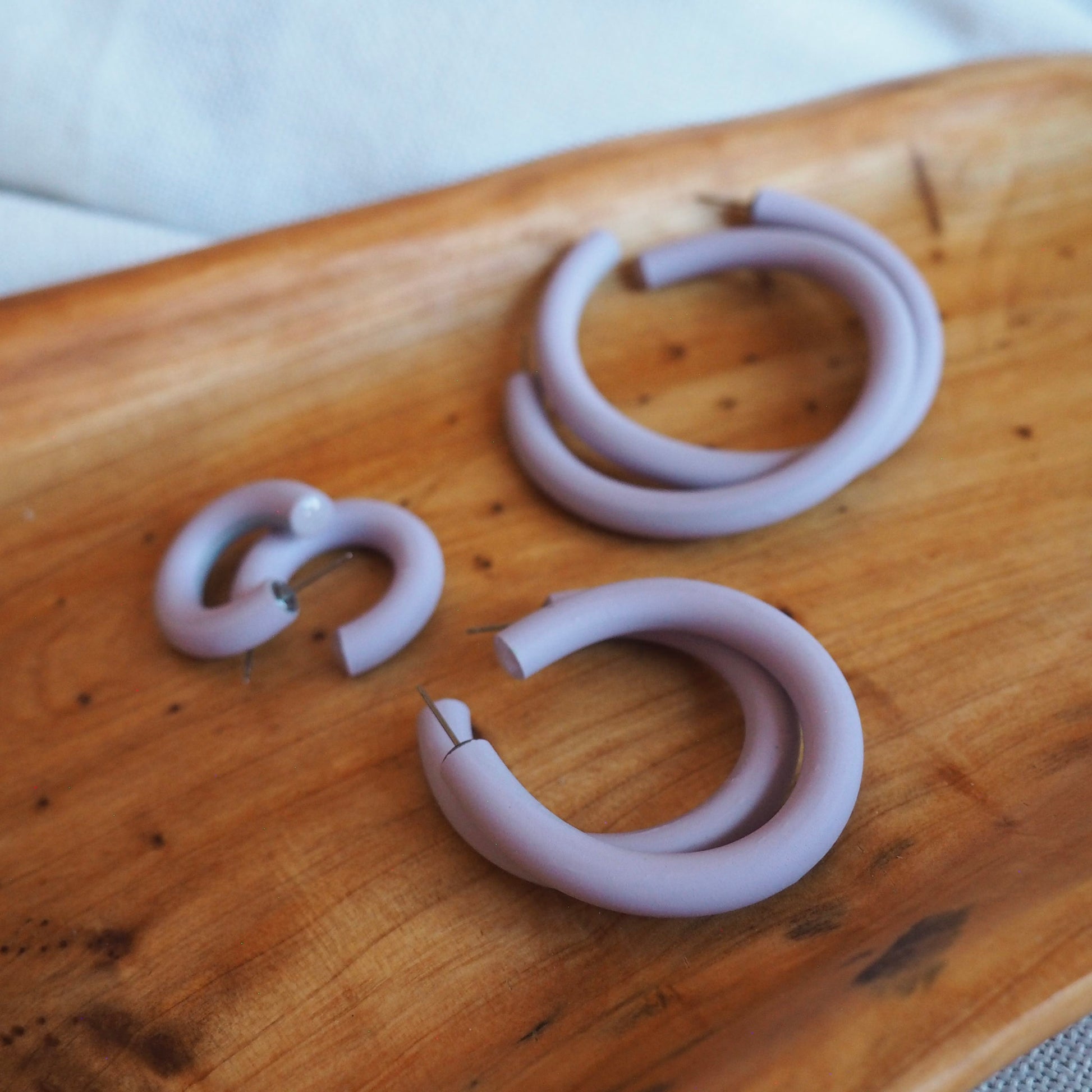 Various sized  lavender polymer clay hoops set on wooden tray on a white textured background. 