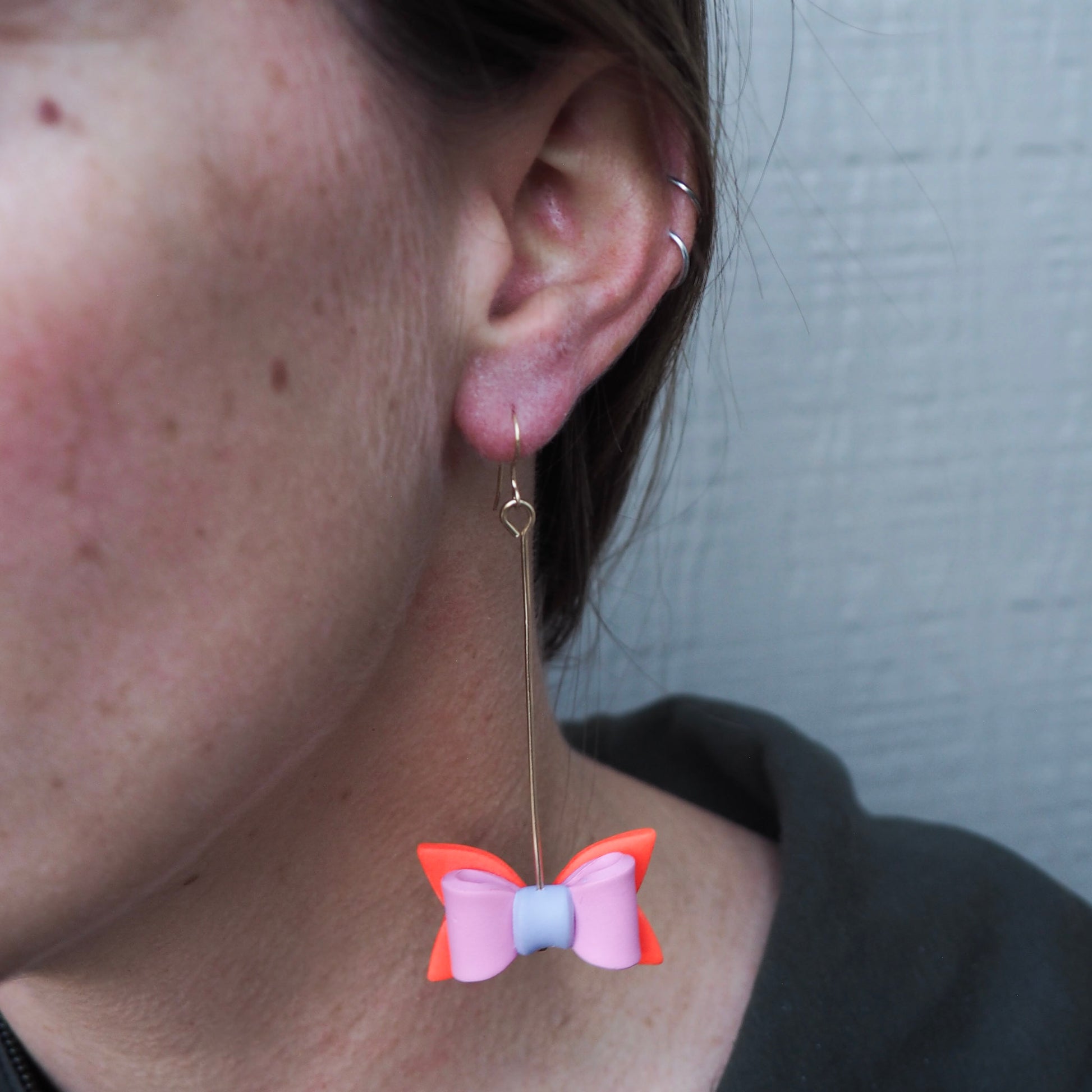 model wearing multicolored bow shaped earrings hung on gold pins with gold fish hooks 