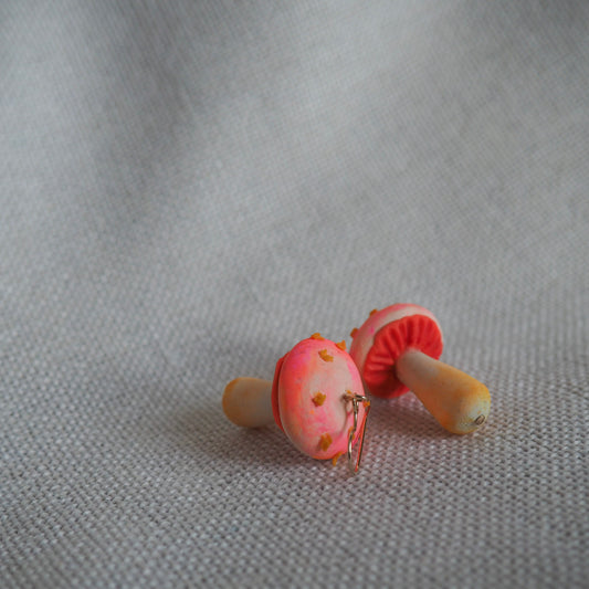 Pair of polymer clay earrings resembling small mushrooms with off white and yellow stems, electric coral/pink caps with yellow scales and gold hooks set on white textured background. 