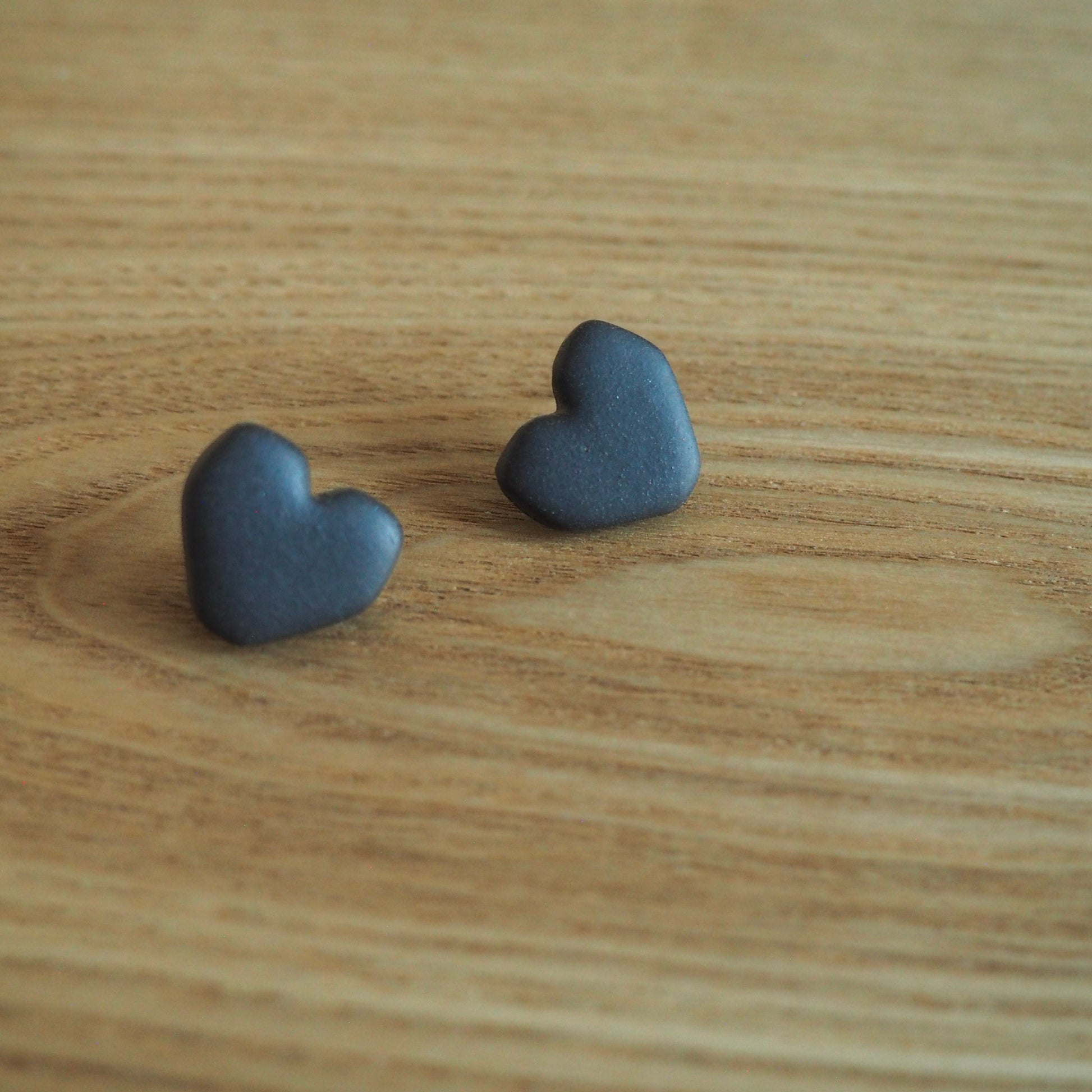 Black geometric heart polymer clay studs set on wood backdrop 