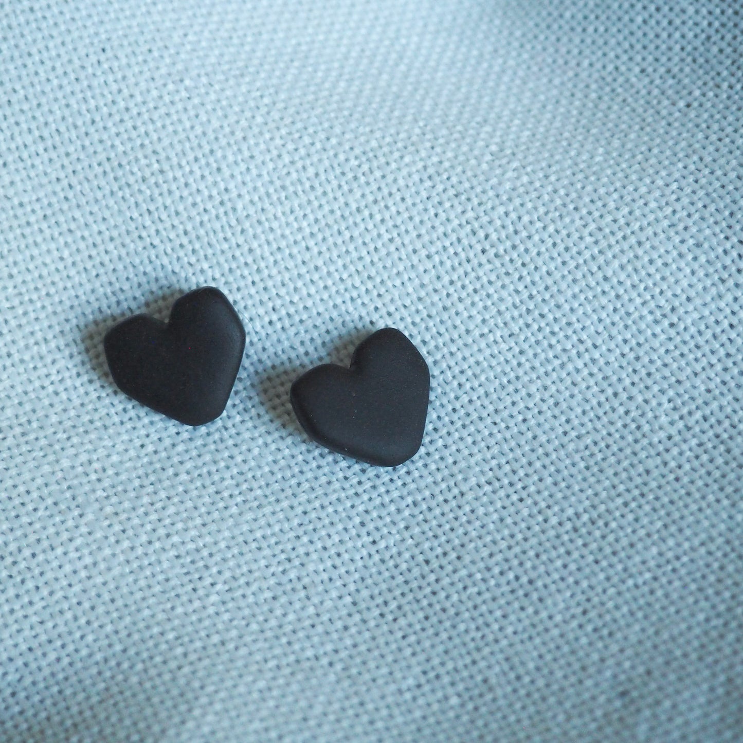 Black geometric heart polymer clay studs set on white textured backdrop