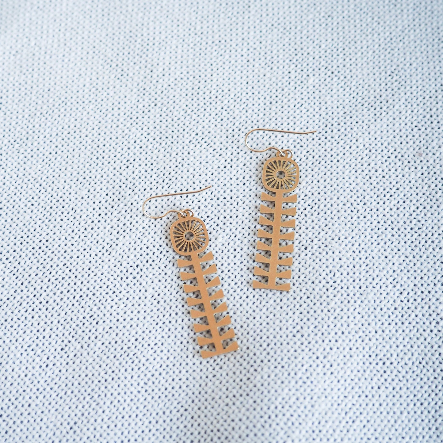 folk style flower earrings made from bass with fish hooks on a white textured background 