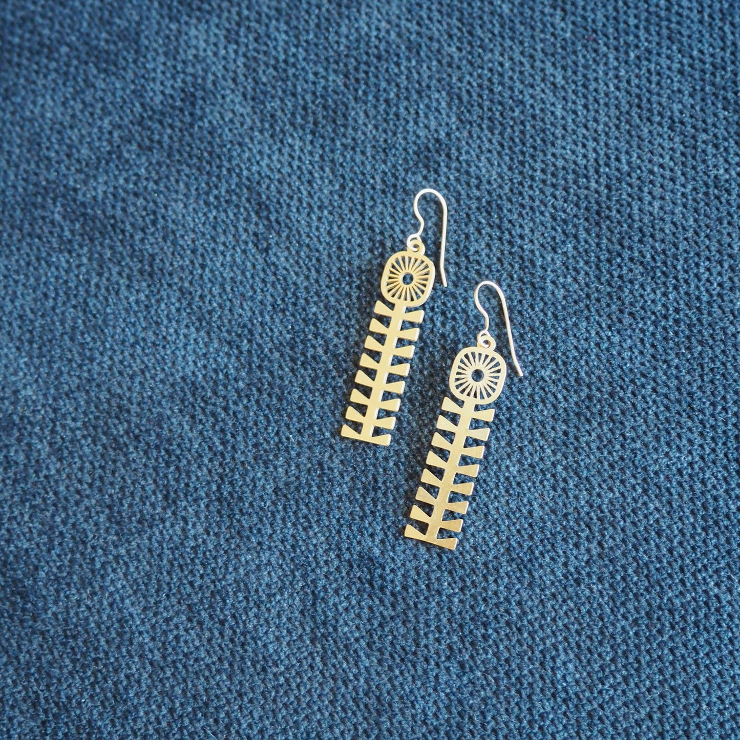 folk style flower earrings made from bass with fish hooks on a navy blue textured background 