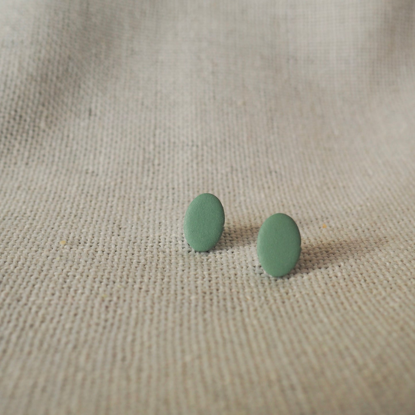 Blue/green polymer clay oval stud earrings set on white textured backdrop 