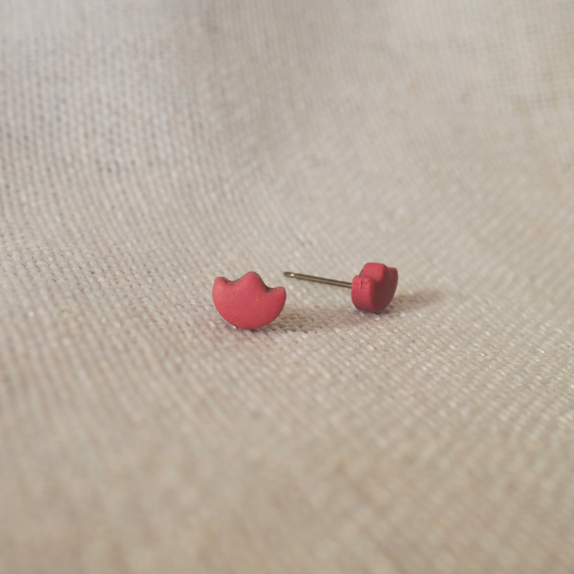 Light cranberry polymer clay tulip top stud earrings set on white textured backdrop 