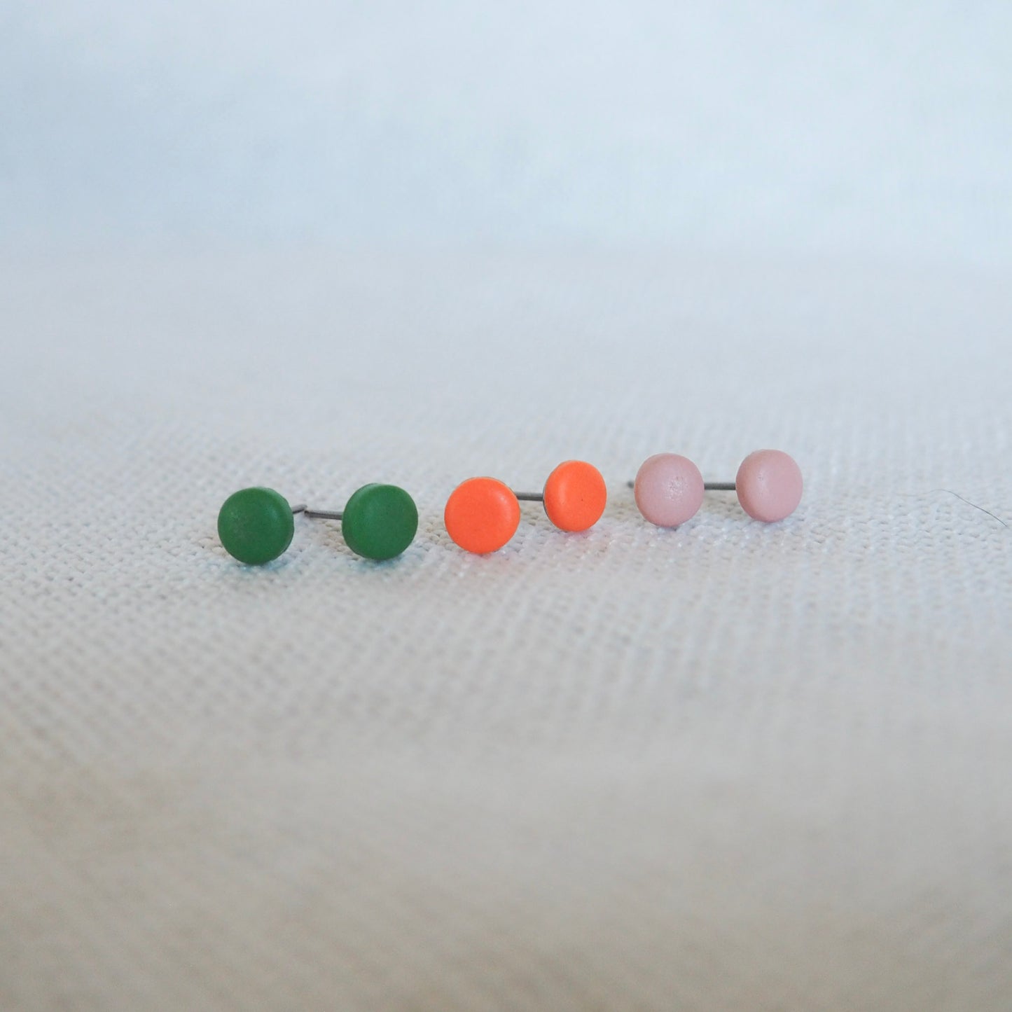 3 pairs of small circle clay studs in green, bright orange, and light pink on a white neutral background 