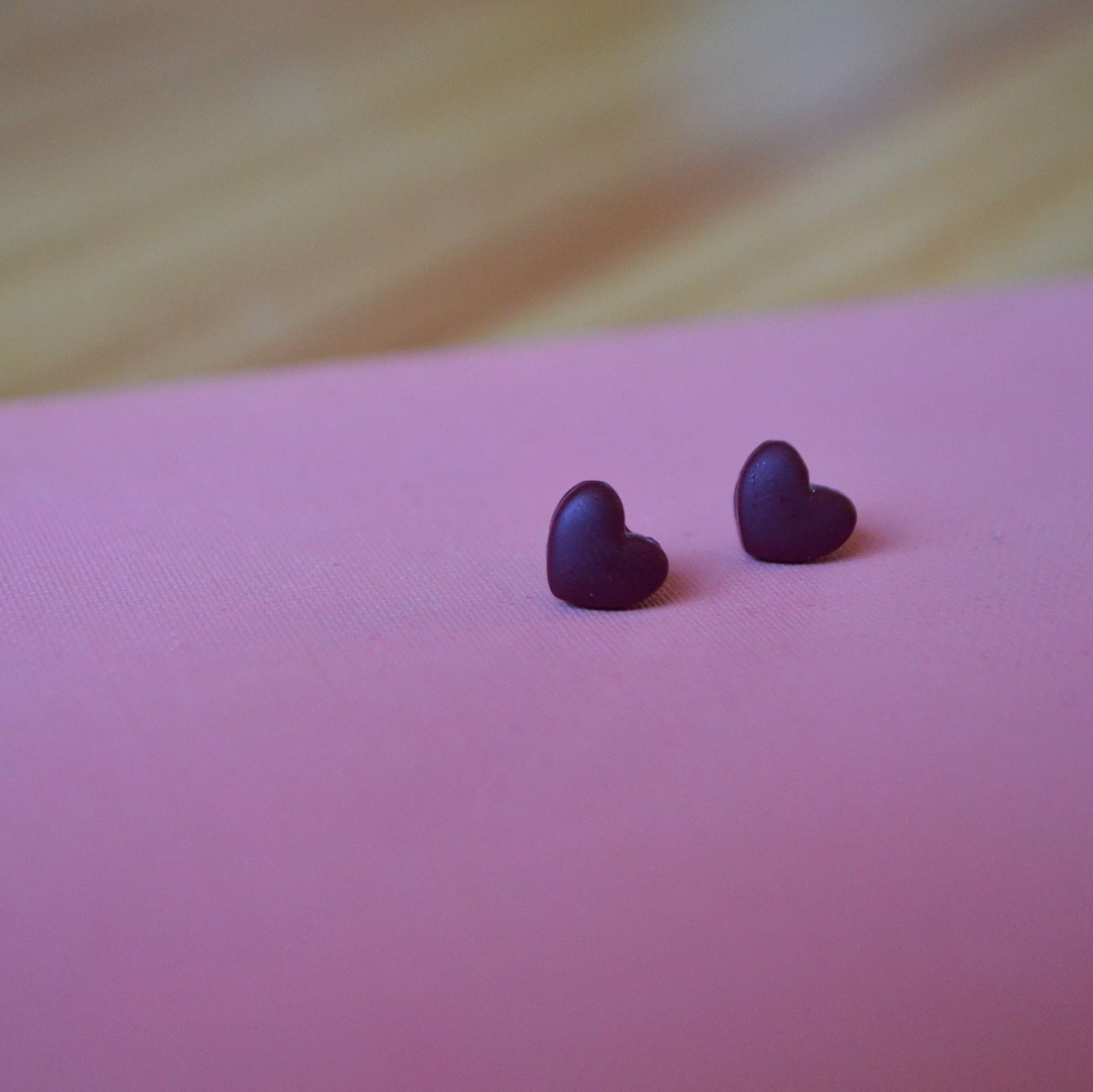 Small cranberry heart polymer clay stud earrings on light pink backdrop 