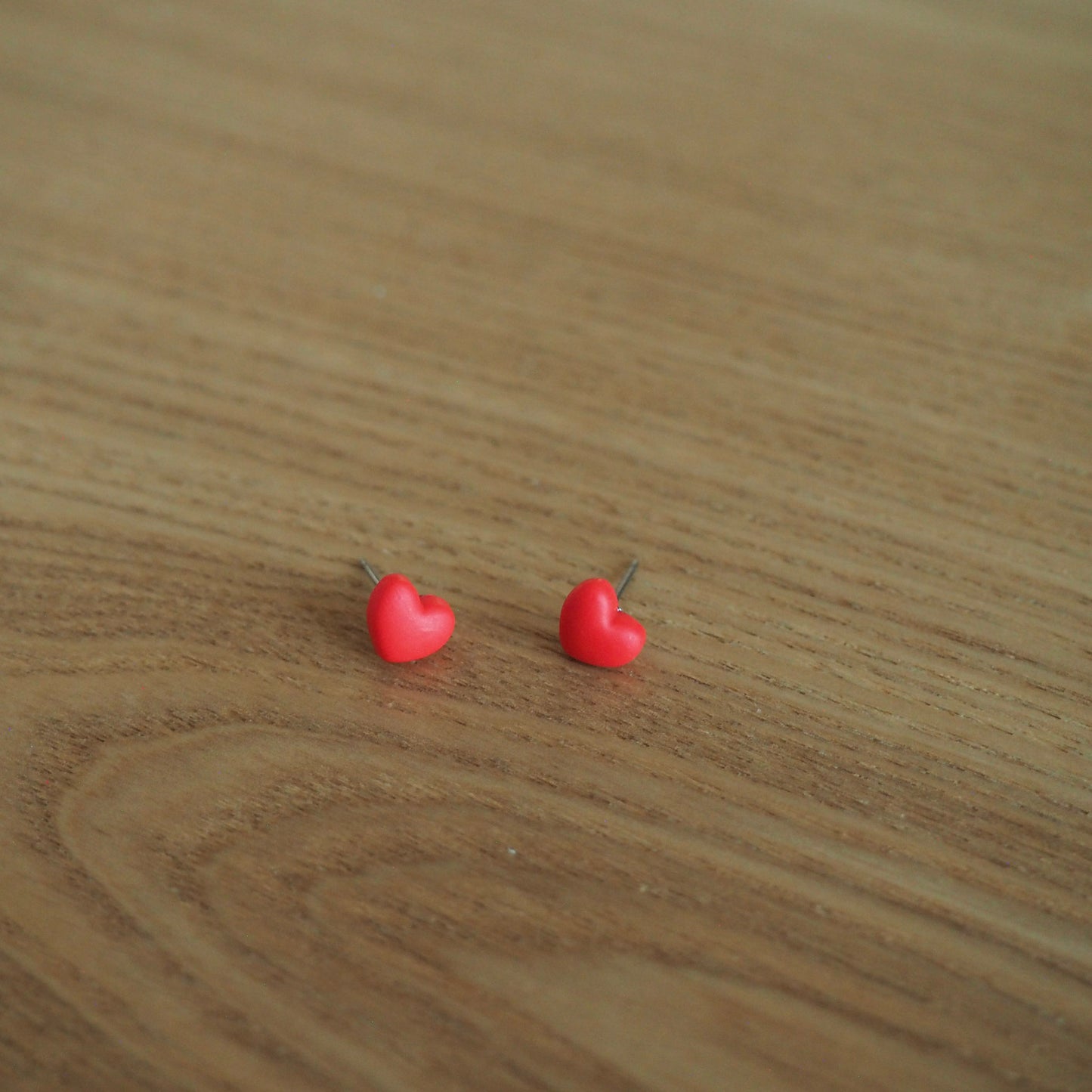 Small red heart polymer clay stud earrings on wood backdrop 
