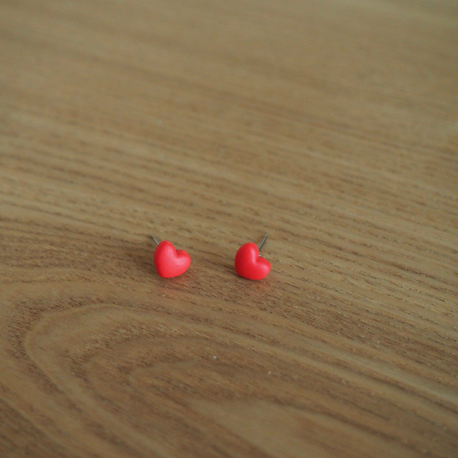 Small red heart polymer clay stud earrings on wood backdrop 