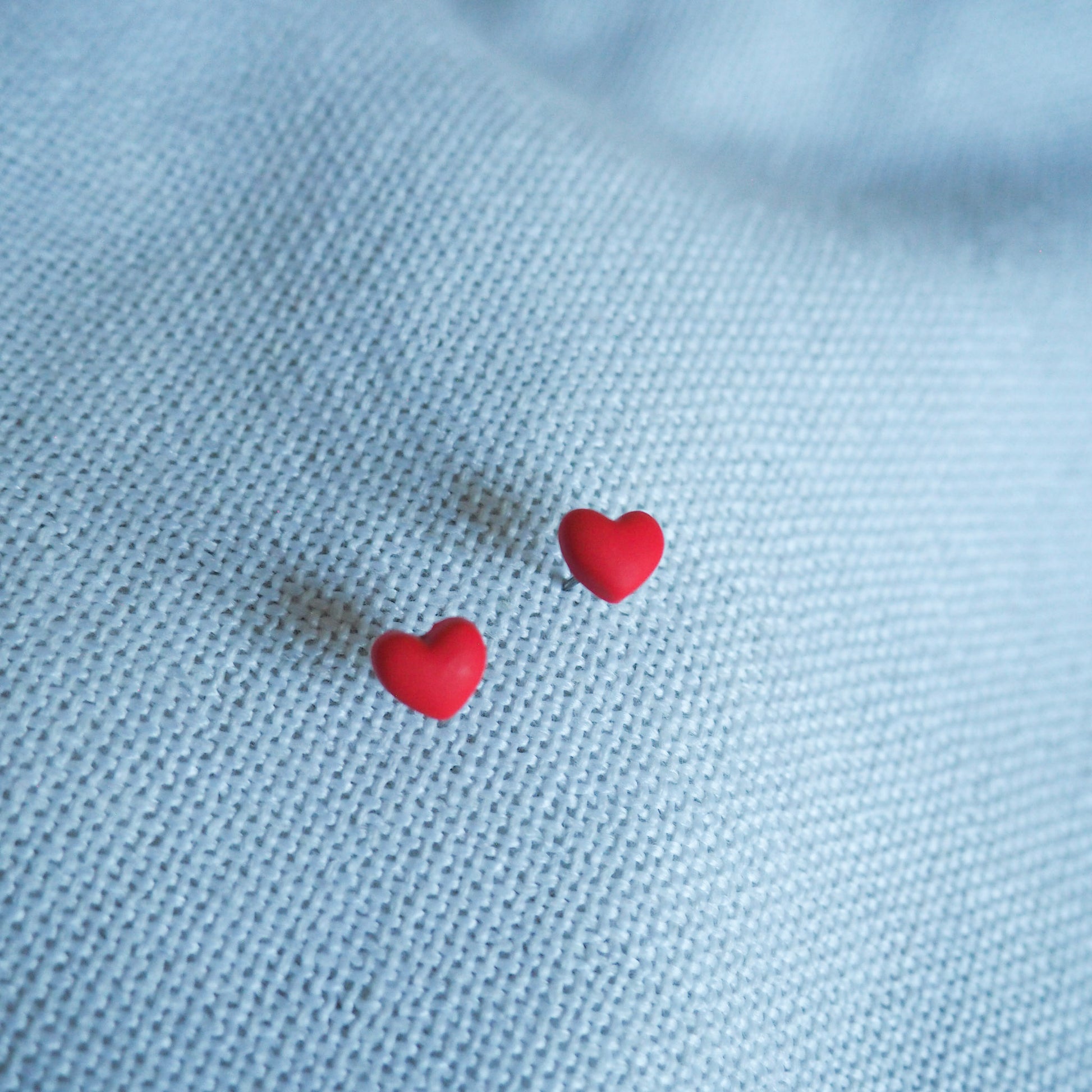 Small red heart polymer clay stud earrings on white textured backdrop 