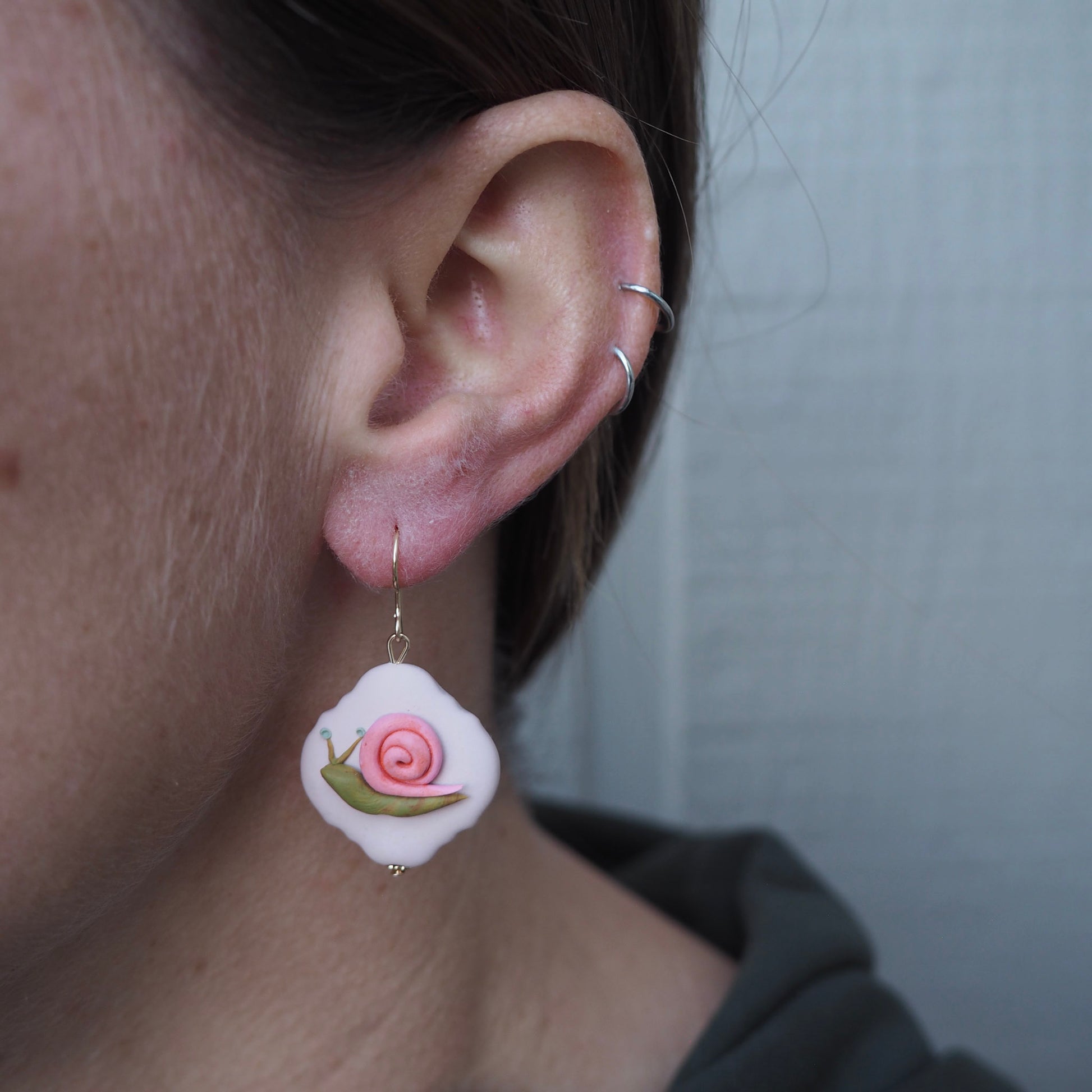 model wearing polymer clay earrings with gold hooks with green and pink snail on pink translucent background
