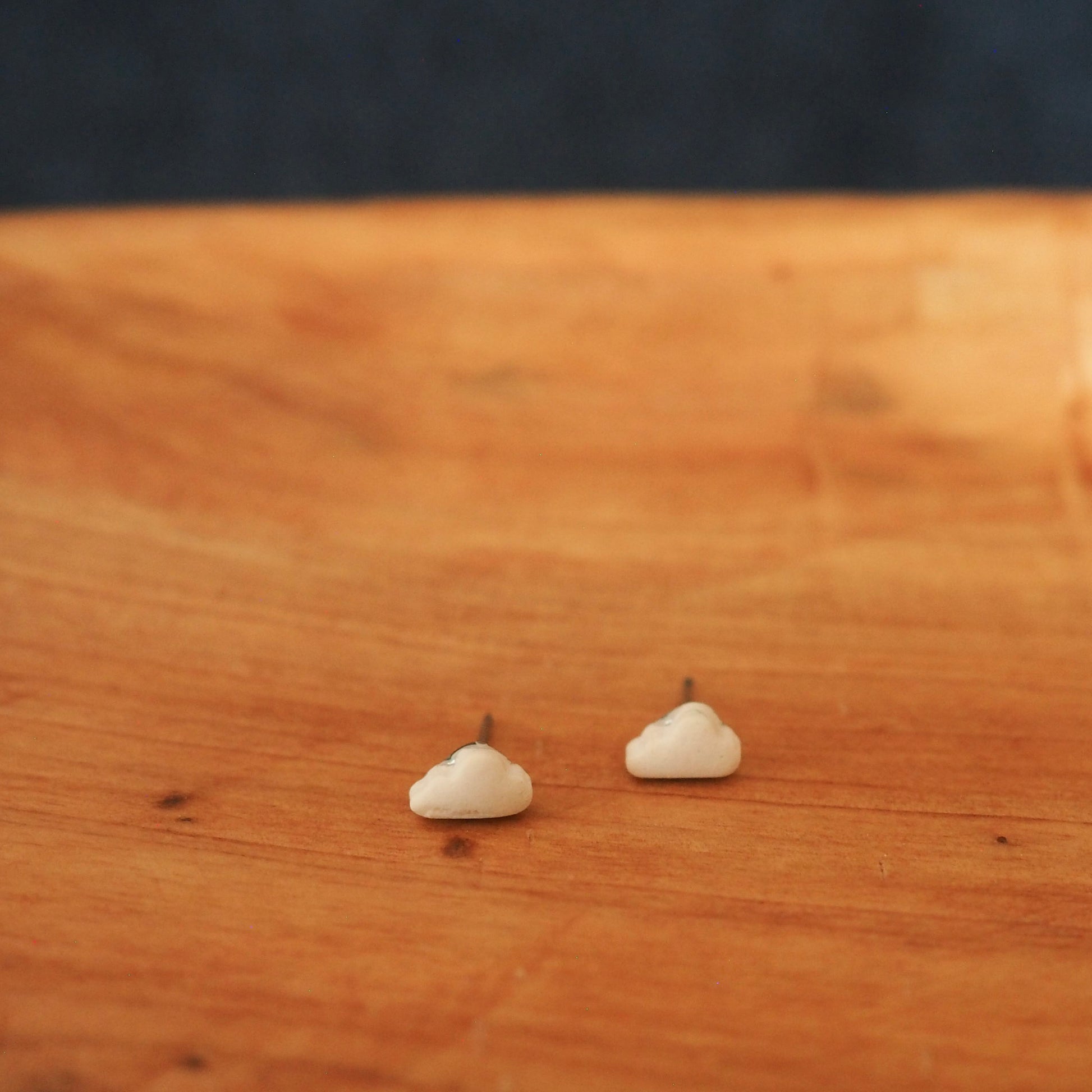 Small white cloud polymer clay stud set in a wooden tray on a dark blue textured background. 