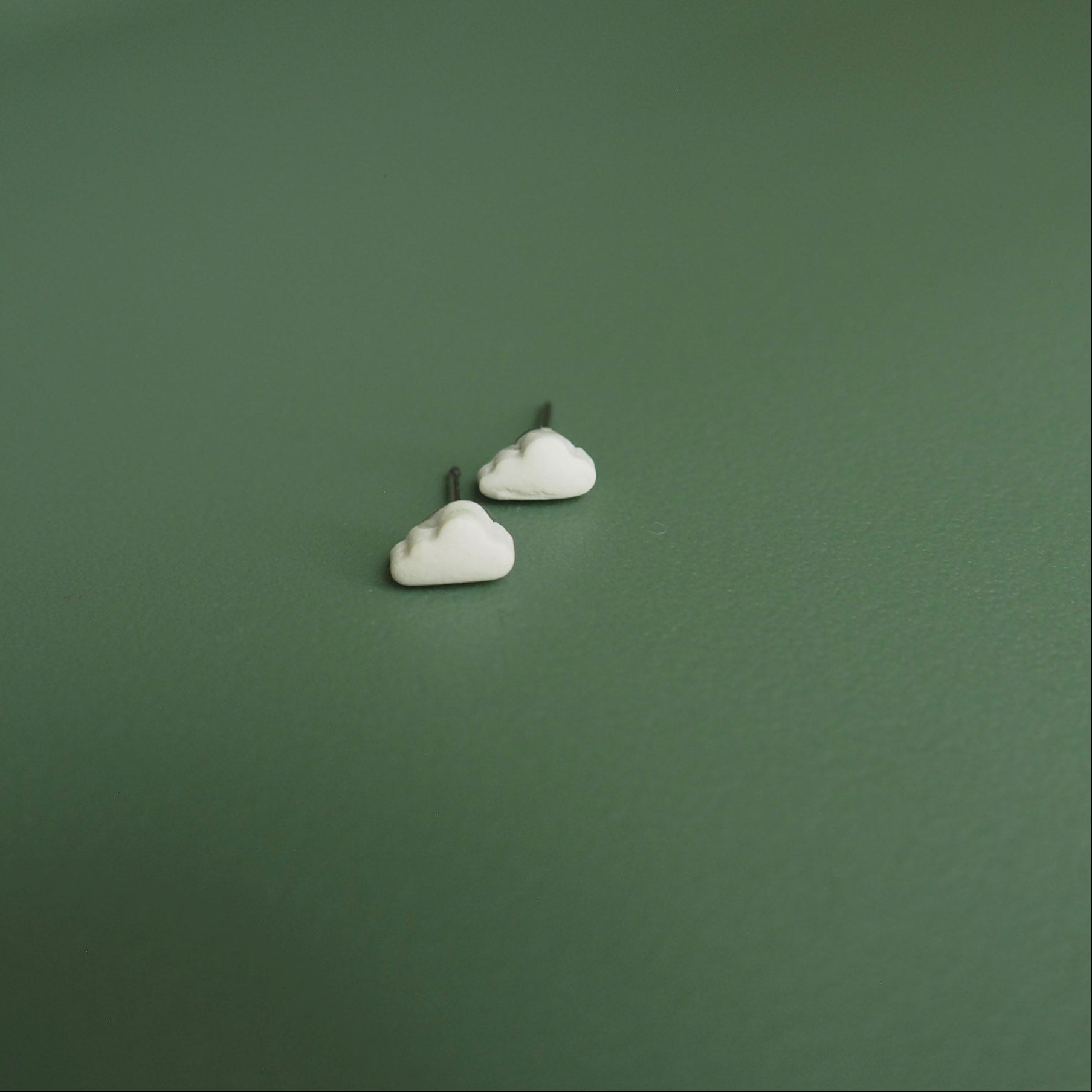 Small white cloud polymer clay studs set on a green background. 
