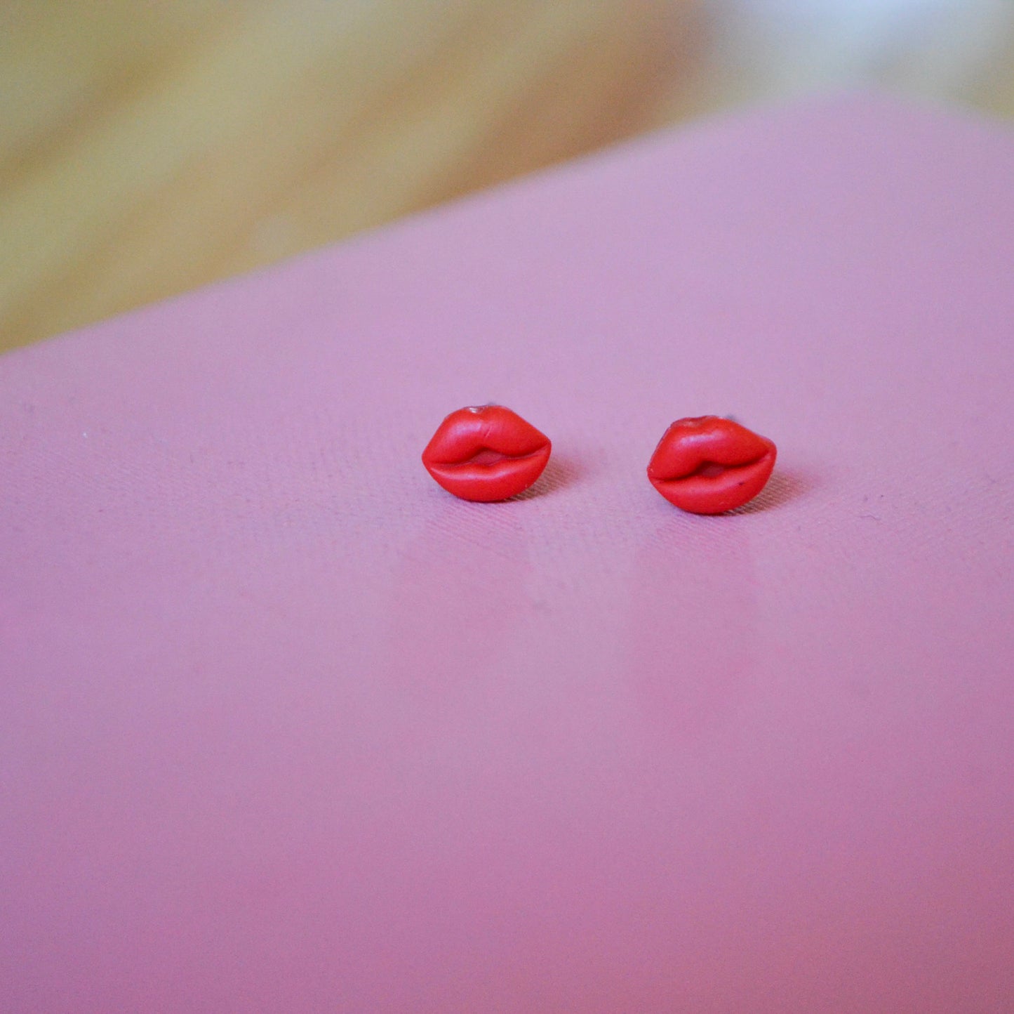 clay lip shaped stud earrings with titanium posts and backs on a pink backdrop
