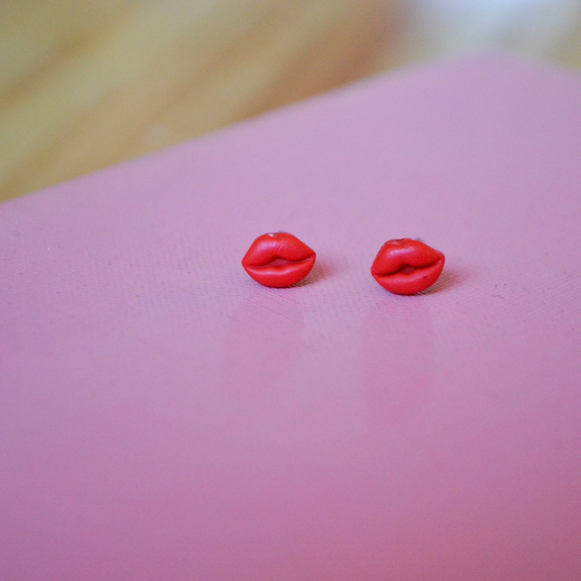 clay lip shaped stud earrings with titanium posts and backs on a pink backdrop