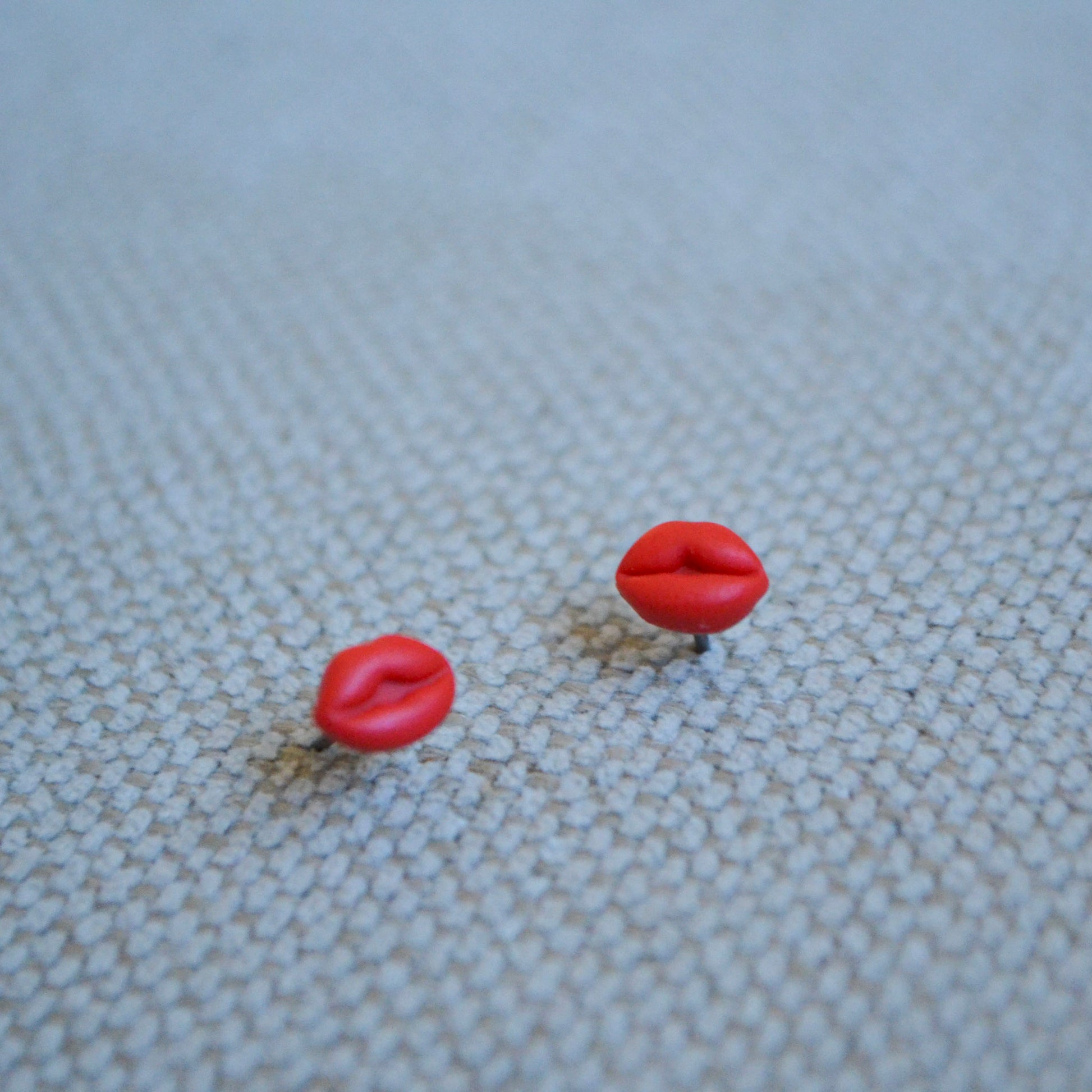 clay lip shaped stud earrings with titanium posts and backs on a white textured backdrop