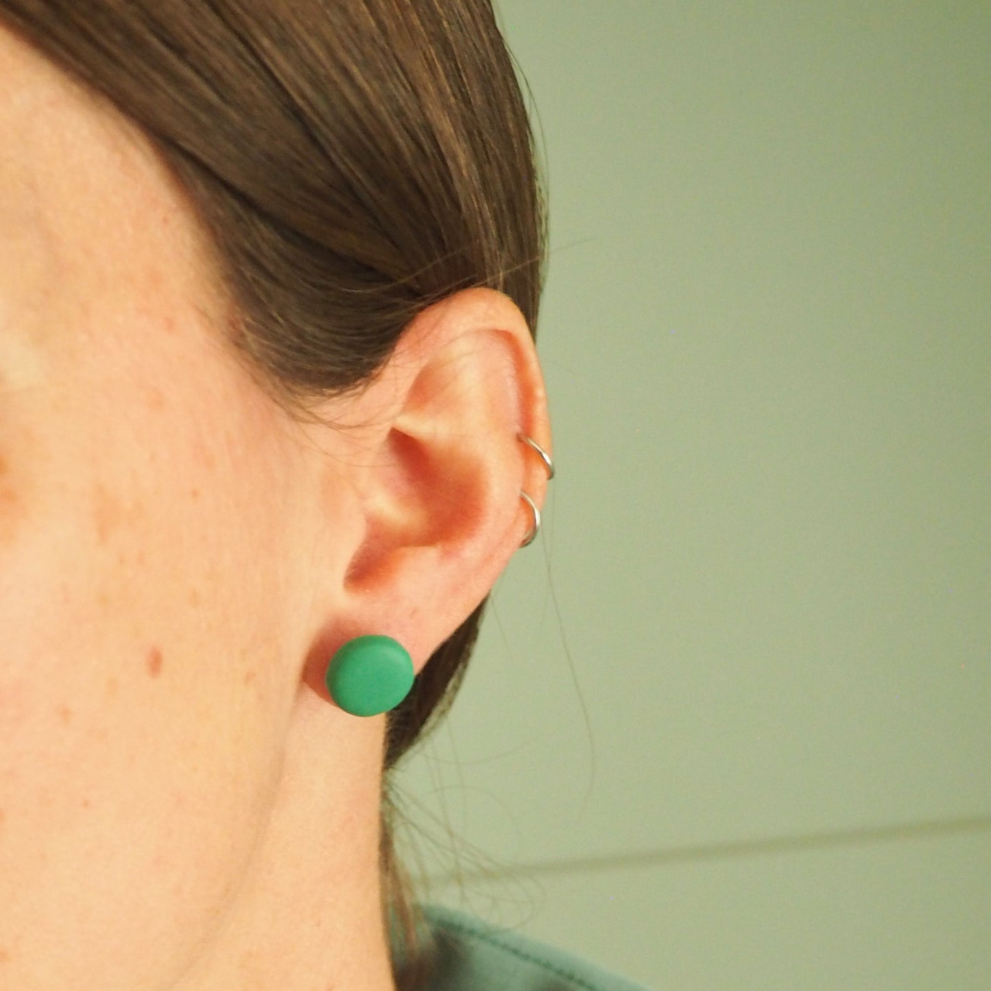 Model wearing a bright green clay stud on a green background 