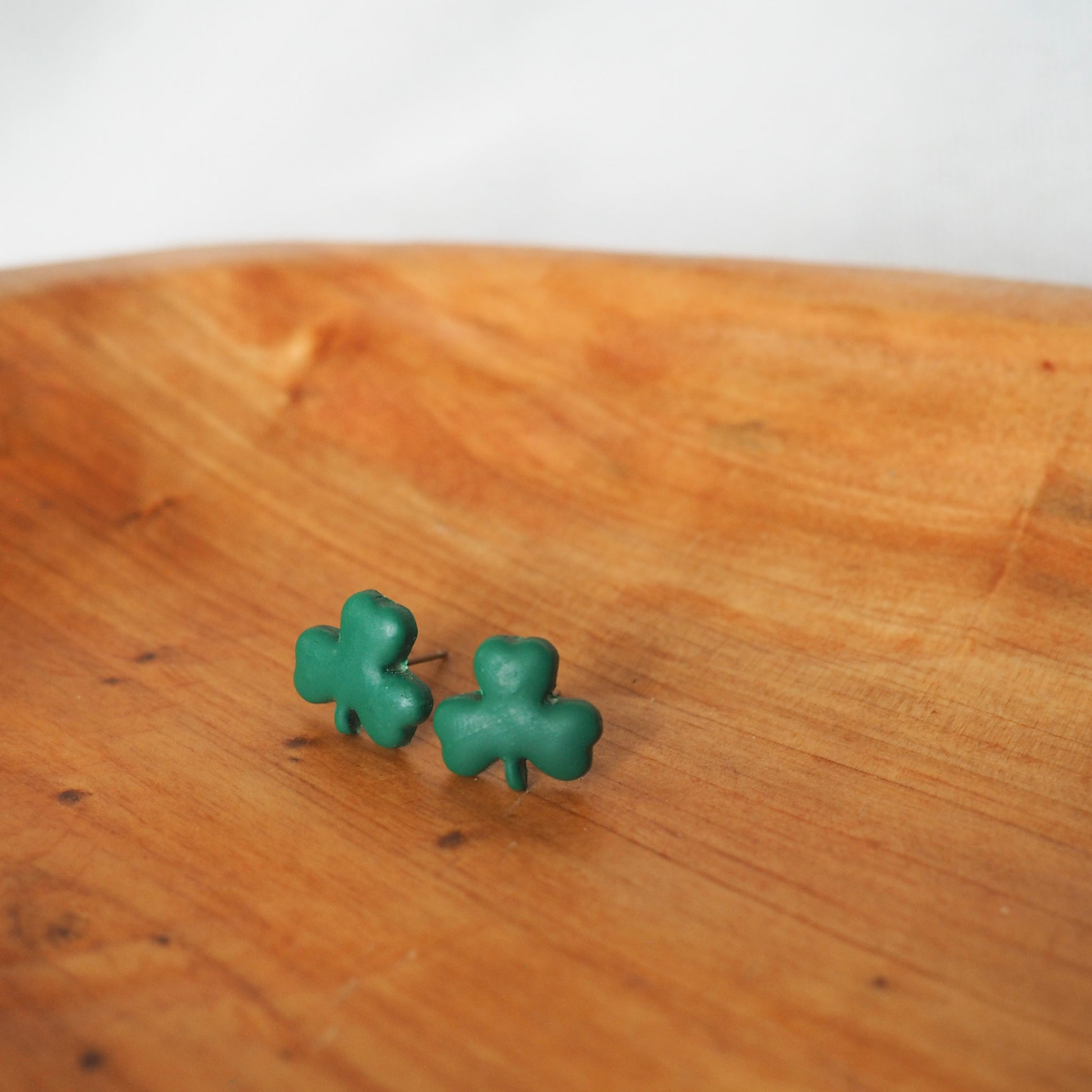 Small green shamrock polymer clay stud set in a wooden tray on a white textured background. 